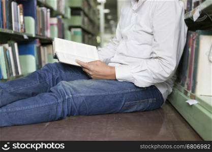 man sitting and reading book on floor in aisle in library