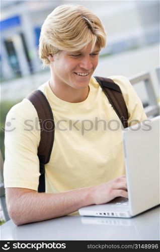 Man sitting at table outdoors with laptop smiling (selective focus)