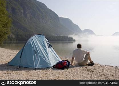 Man sitting beside his tent at a mountain lake