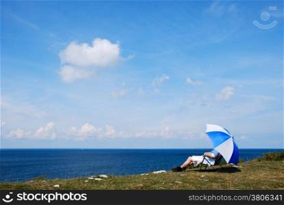 Man sitting in a chair relaxing under an umbrella at seaside with a beautiful view by the Baltic Sea in Sweden