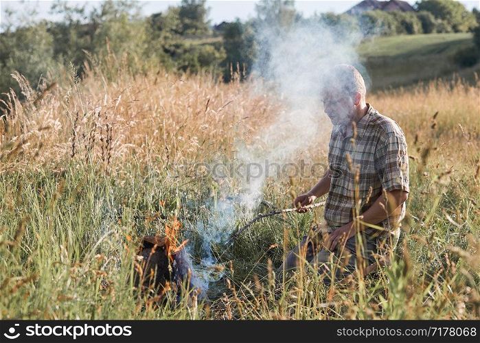 Man sitting in a grass beside a campfire on a meadow. Candid people, real moments, authentic situations