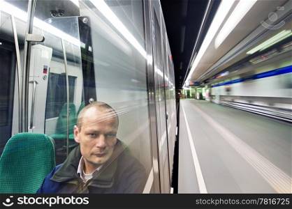Man, sitting in a metro at night, passing a station, looking out the window with a weary and tired look in his eyes