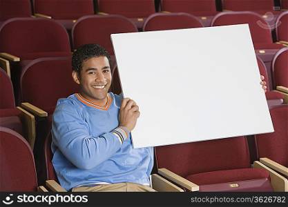 Man sitting in auditorium, holding empty placard