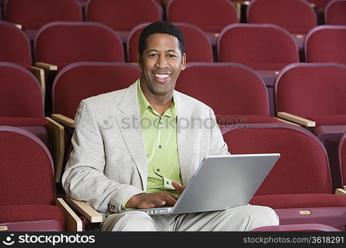 Man sitting in auditorium with laptop, portrait