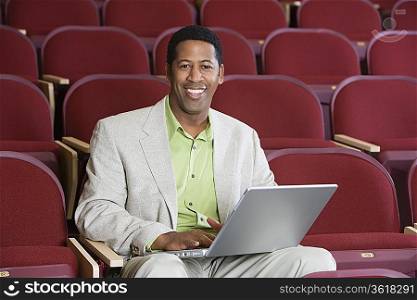 Man sitting in auditorium with laptop, portrait