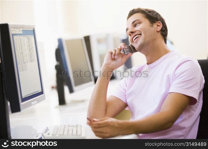 Man sitting in computer room using cellular phone and smiling