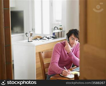 Man sitting in kitchen using phone elevated view