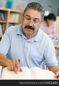 Man sitting in library with a book and notepad (selective focus)
