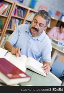 Man sitting in library with a book and notepad (selective focus)