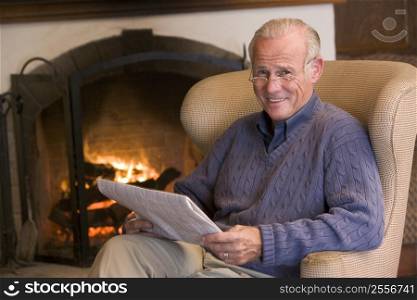 Man sitting in living room by fireplace with newspaper smiling
