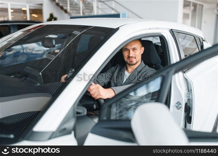 Man sitting in new car, showroom. Male customer choosing vehicle in dealership, automobile sale, auto purchase. Man sitting in new car, showroom