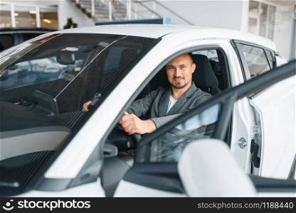 Man sitting in new car, showroom. Male customer choosing vehicle in dealership, automobile sale, auto purchase. Man sitting in new car, showroom