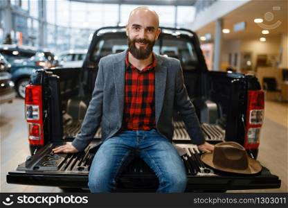 Man sitting in the back of new pickup truck in car dealership. Customer in vehicle showroom, male person buying transport, auto dealer business. Man sitting in the back of truck, car dealership