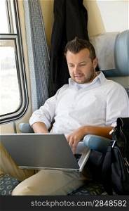 Man sitting in train using laptop computer commuting from work