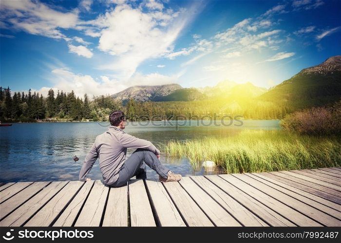Man sitting near alpine mountain lake at summer day