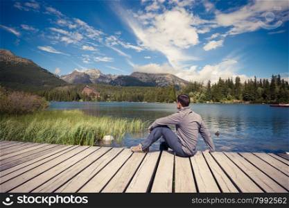 Man sitting near alpine mountain lake at summer day