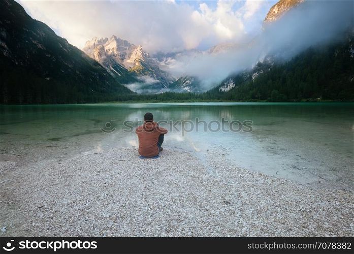Man sitting near mountain lake at cloudy morning. Lago di Landro, Dolomites Alps, Italy