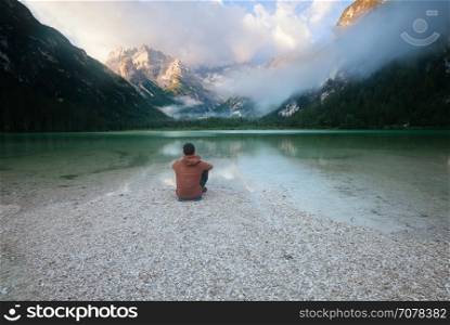 Man sitting near mountain lake at cloudy morning. Lago di Landro, Dolomites Alps, Italy