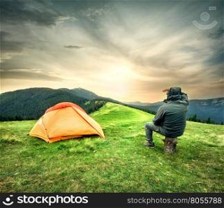 Man sitting near tent looking at the setting sun over mountains. Man sitting near tent looking at the setting sun