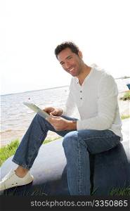 Man sitting on a lakeside with electronic tablet
