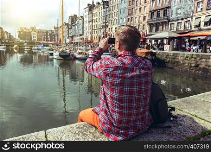 man sitting on a pier and taking a shot of Honfleur harbor with his smartphone