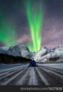 Man sitting on a snowy road looking at northern lights