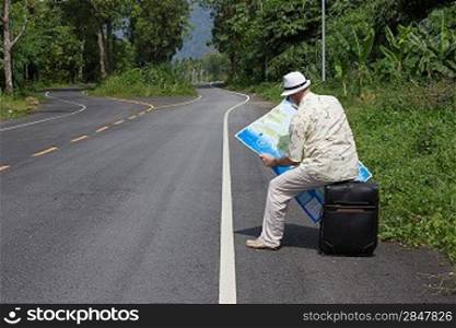 man sitting on a suitcase on the side of the road and look at the map