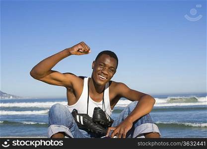 Man sitting on beach with with football boots round his neck cheering