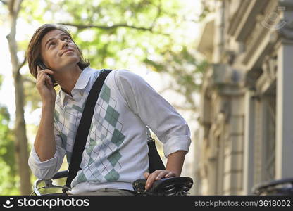 Man sitting on bicycle, talking on mobile phone and looking up