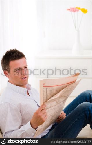 Man sitting on couch at home reading reading newspaper .