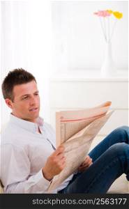 Man sitting on couch at home reading reading newspaper .