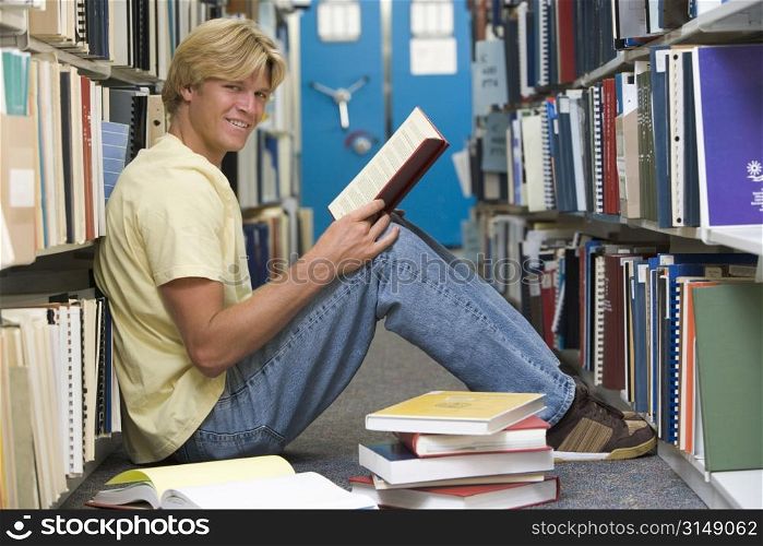 Man sitting on floor in library holding book