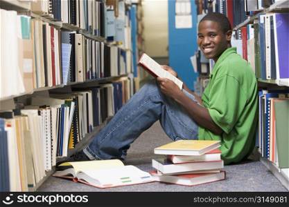 Man sitting on floor in library holding book