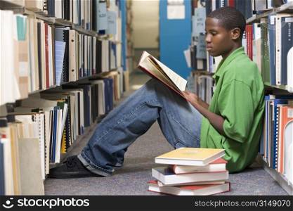 Man sitting on floor in library reading book