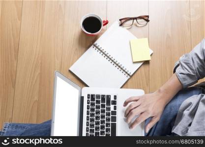 man sitting on floor with laptop computer, coffee cup and eyeglasses - top view