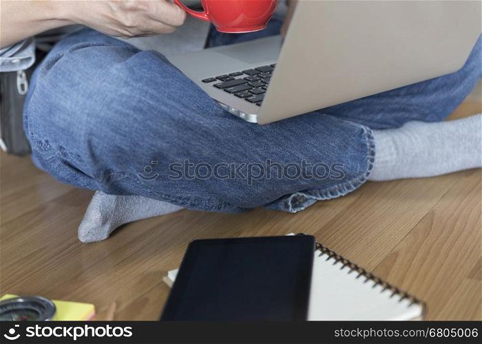 man sitting on floor with laptop computer, coffee cup and tablet