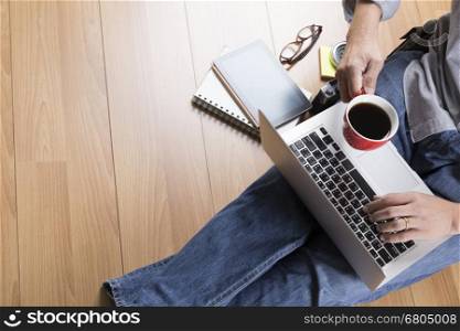 man sitting on floor with laptop computer, coffee cup and tablet - top view