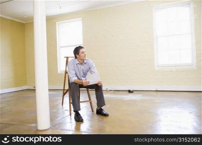 Man sitting on ladder in empty space holding paper
