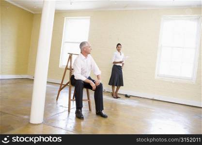 Man sitting on ladder in empty space with woman holding paper