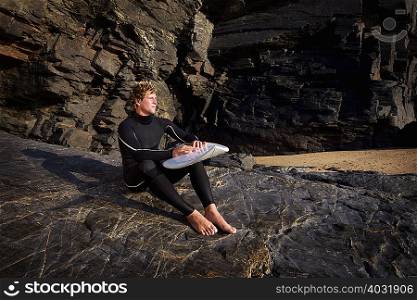 Man sitting on large rock in wetsuit