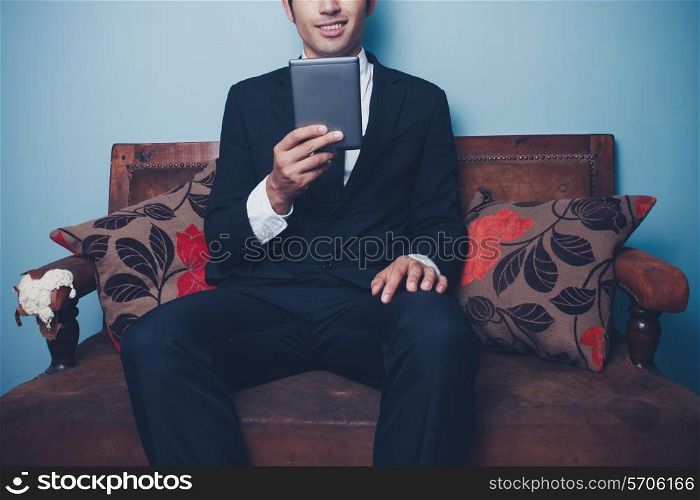 Man sitting on soda and reading on a tablet