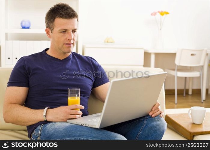 Man sitting on sofa at home and using laptop computer.