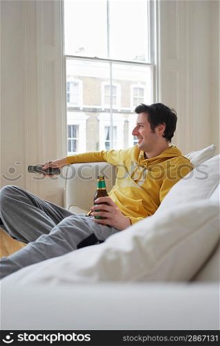 Man sitting on sofa watching television and holding beer bottle