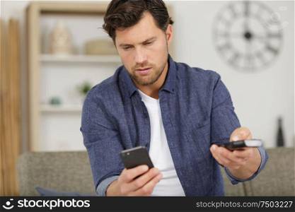 man sitting on sofa with cellphone and tv control