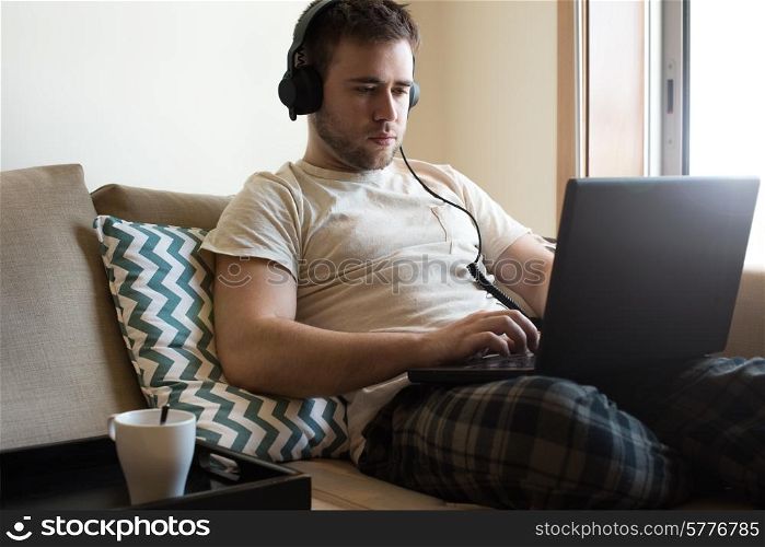 Man sitting on sofa with headphones and laptop