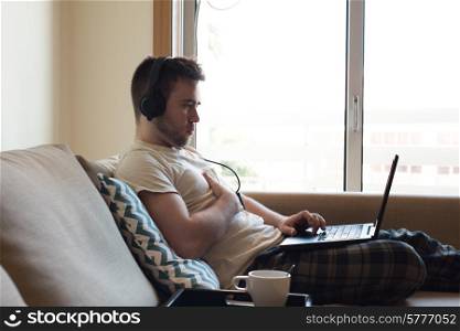Man sitting on sofa with headphones and laptop