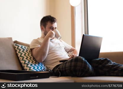 Man sitting on sofa with laptop and a cup of coffee