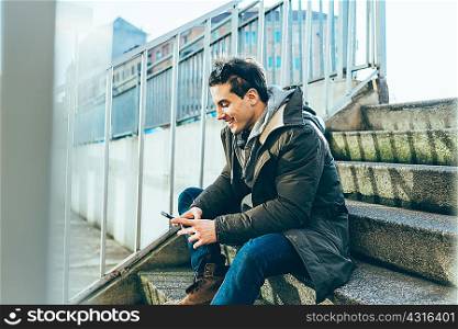 Man sitting on step using smartphone smiling