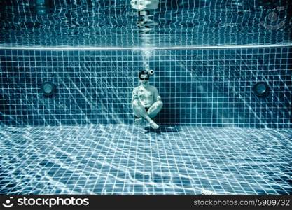 Man sitting on the bottom of the swimming pool under water