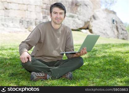 man sitting on the grass working on a laptop